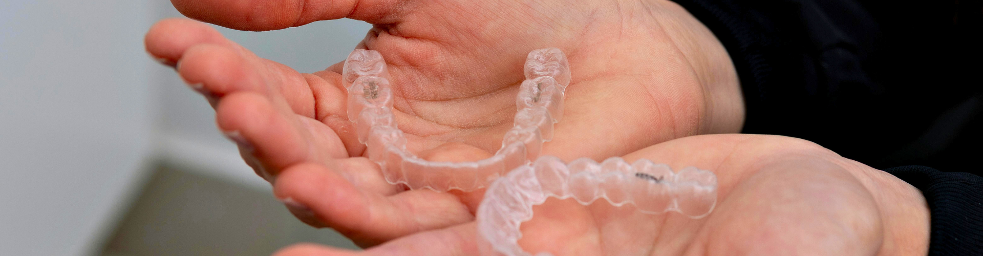 Hands holding clear aligners.